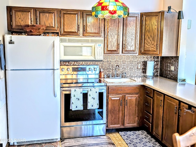 kitchen featuring a sink, decorative backsplash, white appliances, and light countertops