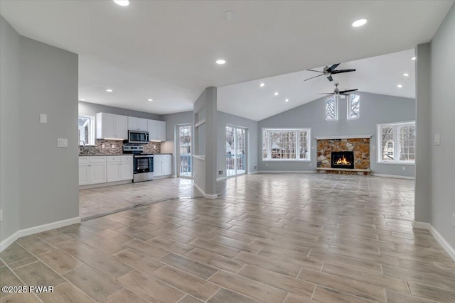 unfurnished living room with a stone fireplace, ceiling fan, and high vaulted ceiling