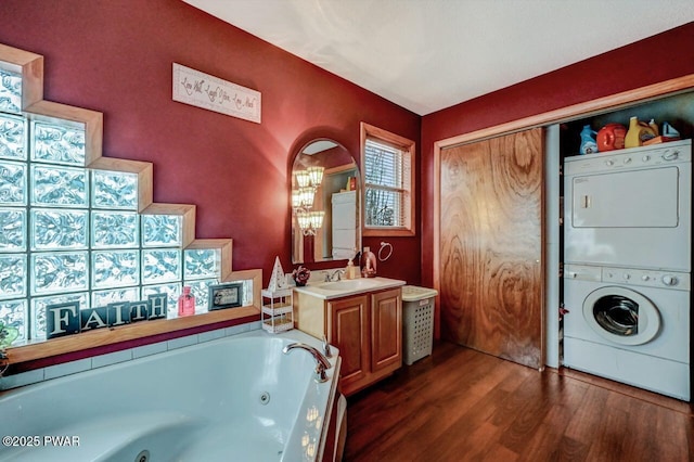 bathroom featuring a tub with jets, vanity, stacked washing maching and dryer, and wood finished floors