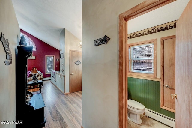 half bathroom featuring lofted ceiling, a baseboard radiator, toilet, wood finished floors, and baseboard heating