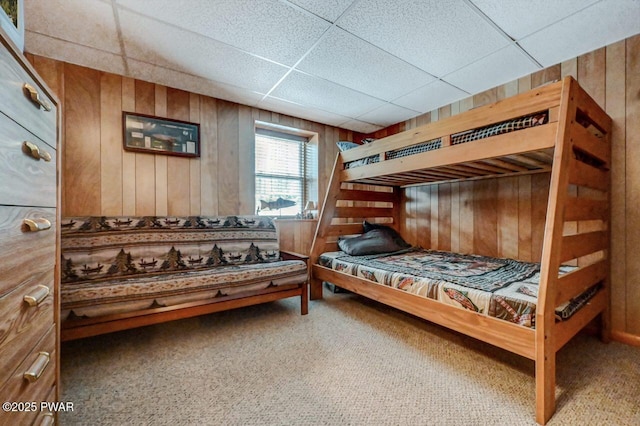 carpeted bedroom featuring a paneled ceiling and wood walls