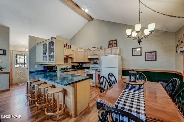 kitchen with white appliances, dark countertops, light wood-type flooring, under cabinet range hood, and beam ceiling