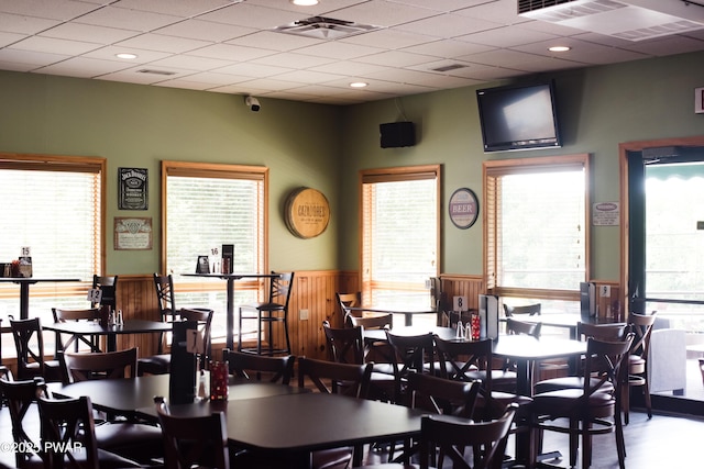 dining space with a wainscoted wall, a drop ceiling, plenty of natural light, and visible vents