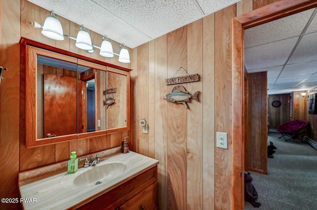 bathroom featuring a paneled ceiling, wooden walls, and vanity