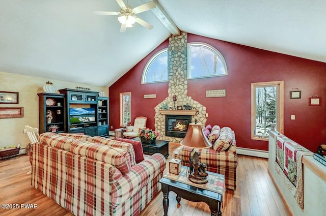 living area featuring beam ceiling, baseboard heating, ceiling fan, a stone fireplace, and wood finished floors