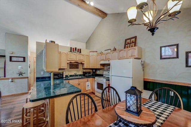 kitchen featuring light brown cabinets, under cabinet range hood, white appliances, beamed ceiling, and dark countertops