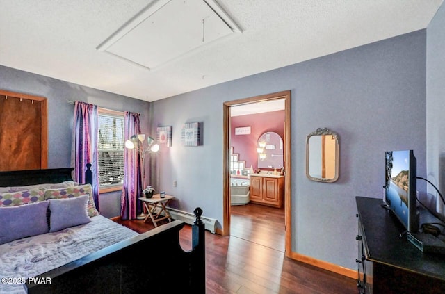 bedroom with connected bathroom, a baseboard heating unit, dark wood-type flooring, baseboards, and attic access