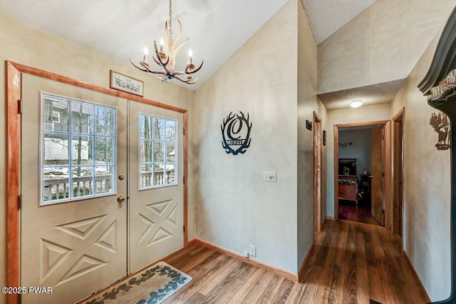 doorway featuring baseboards, a chandelier, wood finished floors, french doors, and high vaulted ceiling