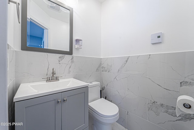 half bath featuring tile walls, visible vents, vanity, and toilet