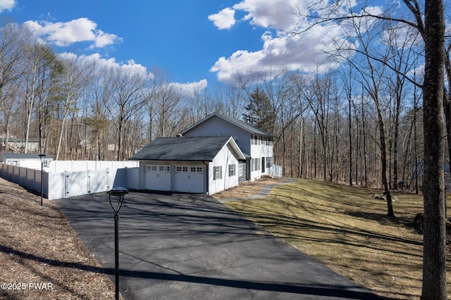 view of side of home featuring aphalt driveway, a garage, fence, a lawn, and a gate