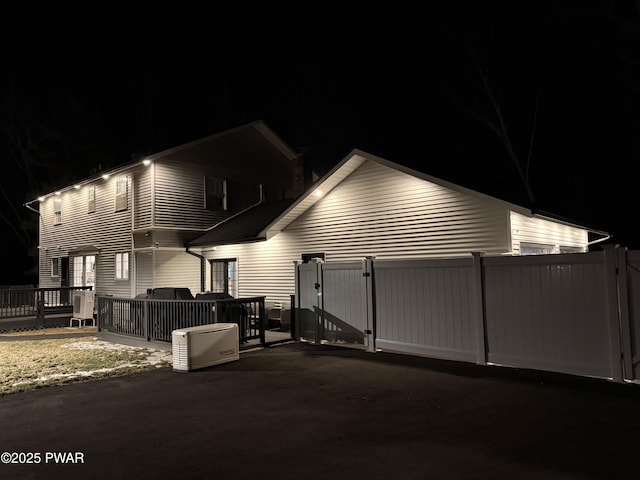 property exterior at night featuring fence and a wooden deck