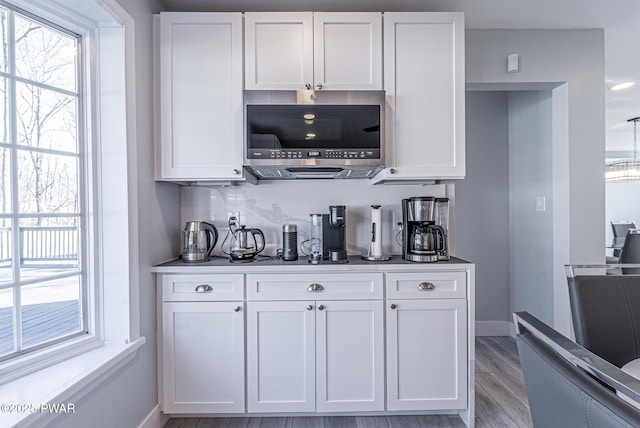 bar featuring light wood-style floors, baseboards, and stainless steel microwave