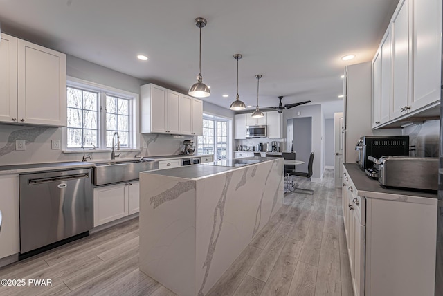 kitchen featuring a sink, white cabinetry, light wood-style floors, appliances with stainless steel finishes, and a center island