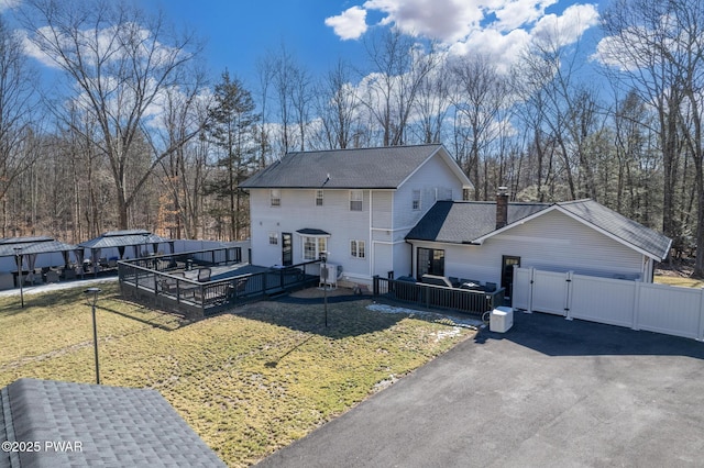 view of front of house with roof with shingles, fence, a wooden deck, and a front lawn