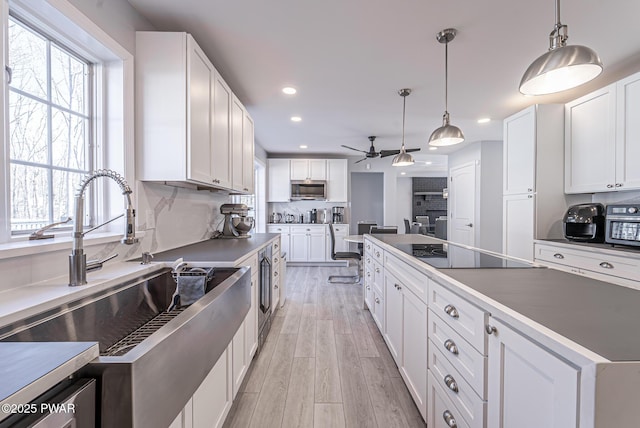 kitchen with light wood-style flooring, stainless steel microwave, black electric stovetop, white cabinetry, and a sink