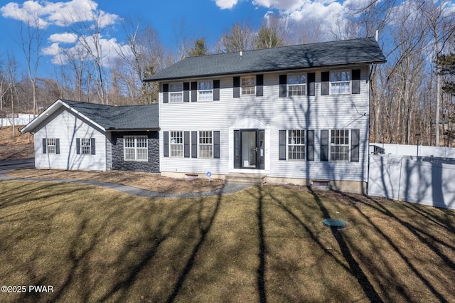 colonial house featuring a front yard, stone siding, and fence