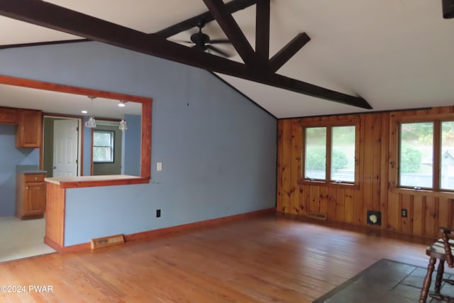 unfurnished living room featuring wood walls, plenty of natural light, lofted ceiling with beams, and light wood-type flooring