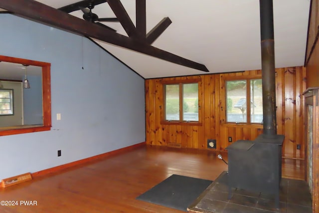 living room featuring a wood stove, wood walls, vaulted ceiling with beams, and hardwood / wood-style flooring