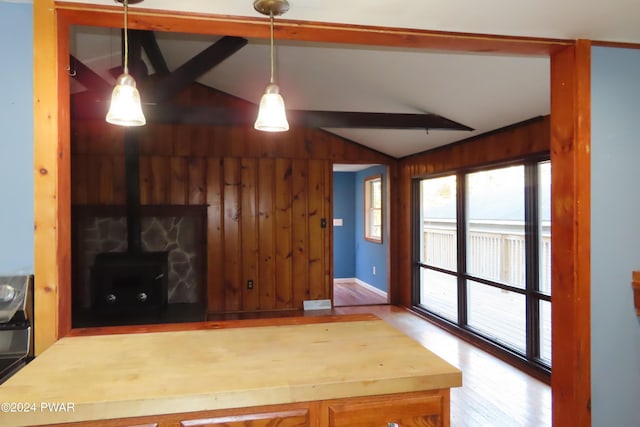 kitchen featuring a wood stove, wooden walls, hardwood / wood-style flooring, vaulted ceiling with beams, and decorative light fixtures