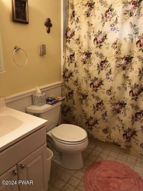 bathroom featuring tile patterned flooring, vanity, toilet, and wooden walls