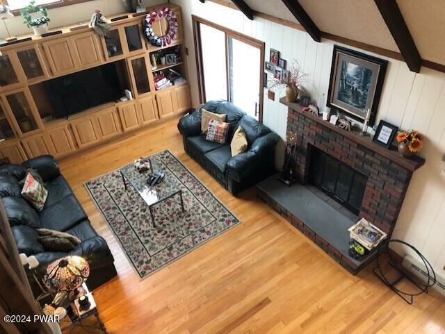 living room with vaulted ceiling with beams, hardwood / wood-style flooring, and a brick fireplace