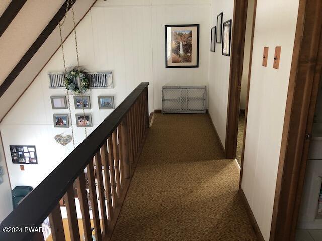 hall featuring dark colored carpet, lofted ceiling with beams, and an inviting chandelier