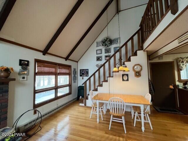 dining space featuring beamed ceiling, high vaulted ceiling, a baseboard heating unit, and light wood-type flooring