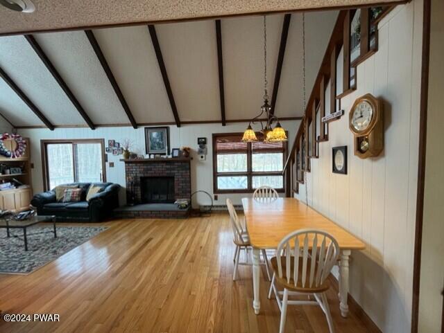 dining room featuring hardwood / wood-style floors, an inviting chandelier, vaulted ceiling with beams, a fireplace, and a healthy amount of sunlight