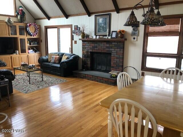 dining space featuring a fireplace, lofted ceiling with beams, and light hardwood / wood-style flooring