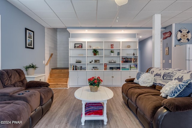 living room with a drop ceiling, built in features, and light wood-type flooring