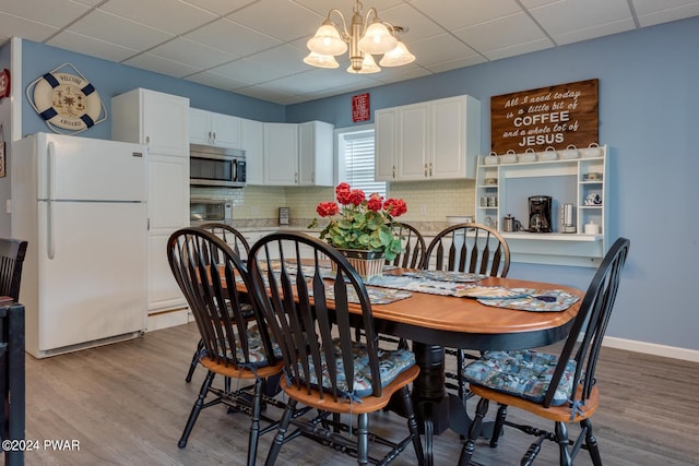 dining area featuring a paneled ceiling, light wood-type flooring, and an inviting chandelier