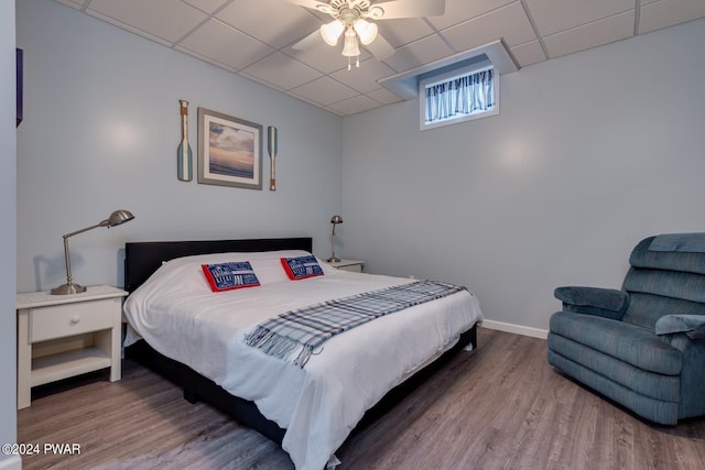 bedroom with ceiling fan, a drop ceiling, and hardwood / wood-style flooring