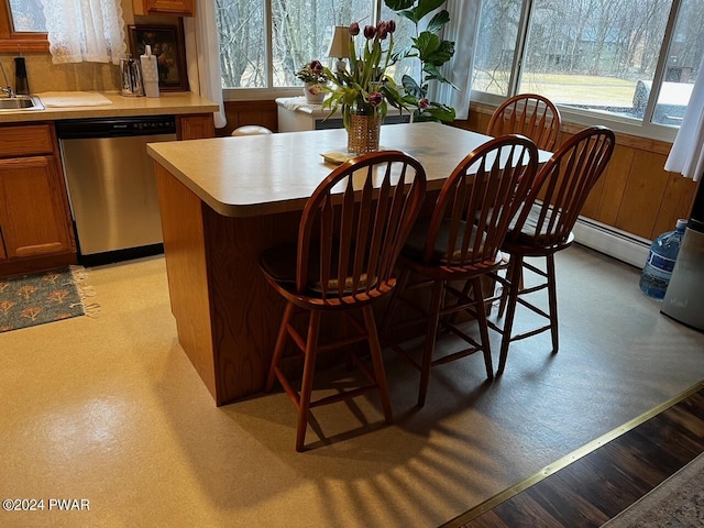 kitchen with a baseboard radiator, stainless steel dishwasher, a wealth of natural light, and a breakfast bar area