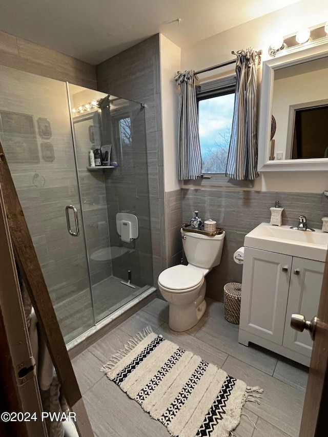 bathroom with tile patterned floors, toilet, vanity, a shower with shower door, and tile walls