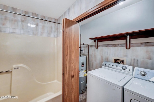 clothes washing area with washing machine and dryer, electric water heater, and tile walls