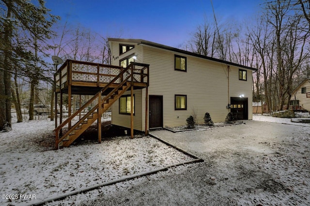 snow covered rear of property featuring a wooden deck and a garage