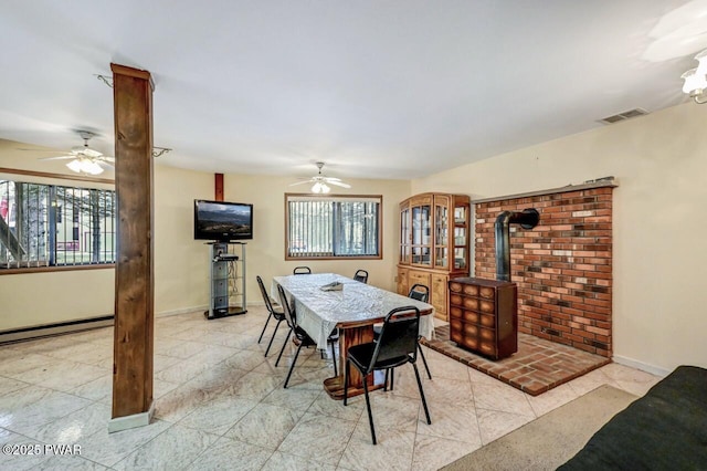 dining area with a wood stove, ceiling fan, and a baseboard radiator