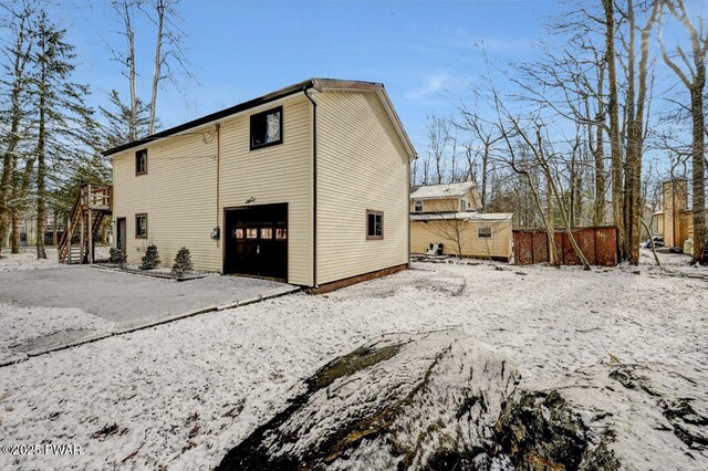 snow covered rear of property featuring a garage and a wooden deck