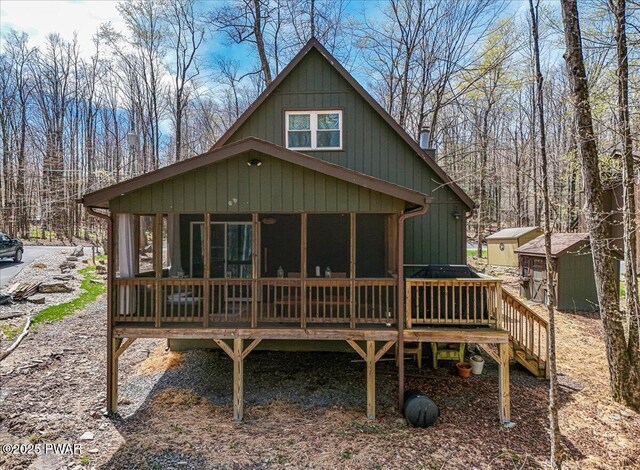 rear view of property featuring a wooden deck, a chimney, a sunroom, and an outbuilding