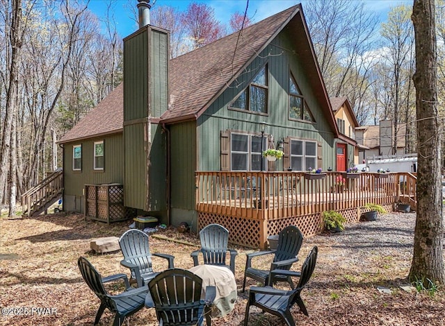 back of house with stairway, a chimney, a shingled roof, a wooden deck, and an outdoor fire pit