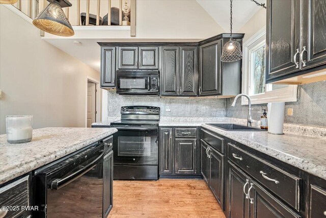 kitchen with tasteful backsplash, a sink, black appliances, light wood-style flooring, and decorative light fixtures