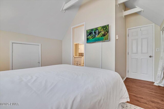 bedroom featuring vaulted ceiling, wood finished floors, and ensuite bathroom