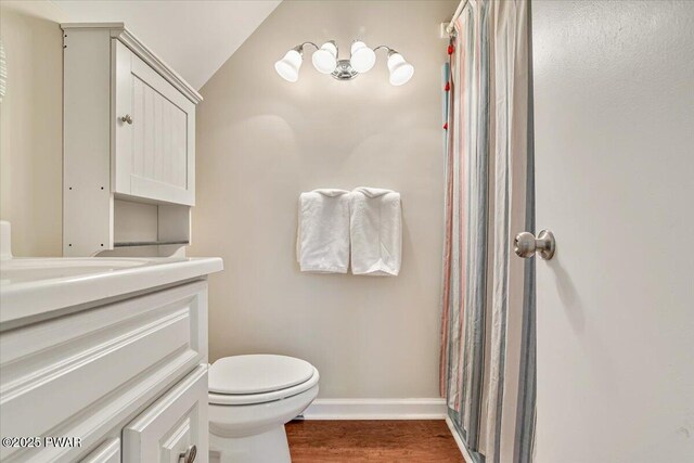 full bath with wood finished floors, vanity, baseboards, toilet, and lofted ceiling