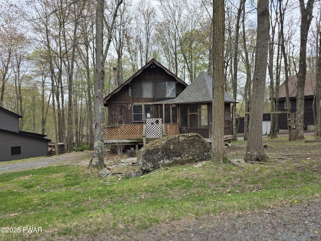 rustic home with a sunroom, a shingled roof, and a front lawn