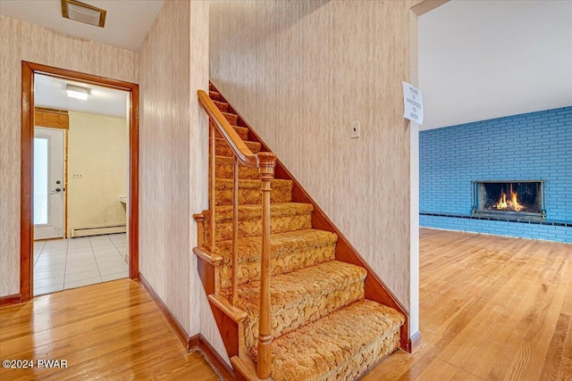 stairway featuring a fireplace, wood-type flooring, and a baseboard heating unit