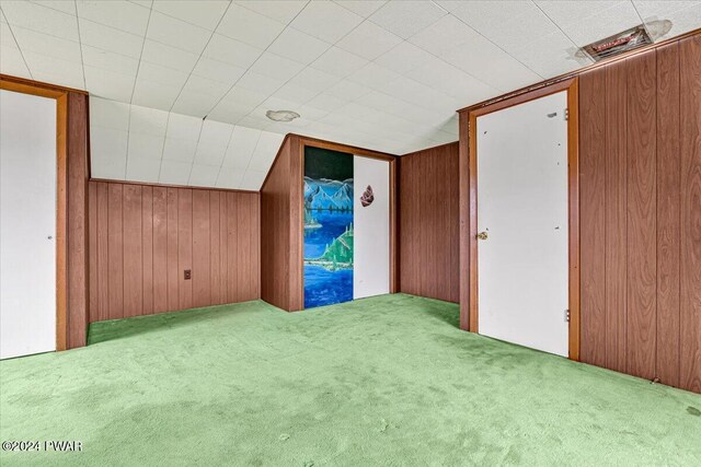 additional living space with lofted ceiling, light colored carpet, and wooden walls