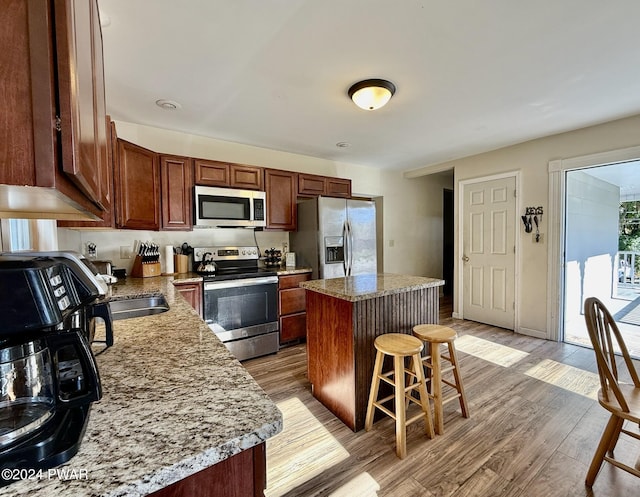 kitchen featuring stainless steel appliances, light stone counters, light hardwood / wood-style flooring, a breakfast bar area, and a kitchen island