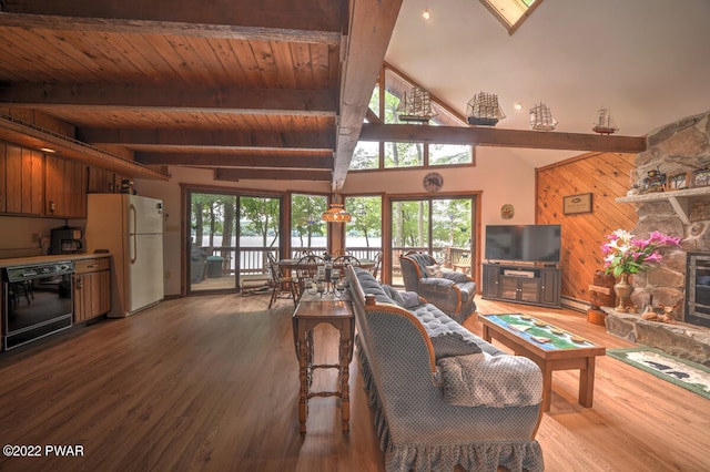 living room with plenty of natural light, wood walls, a stone fireplace, and beam ceiling