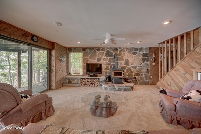 living room with carpet, a wood stove, wooden walls, and ceiling fan