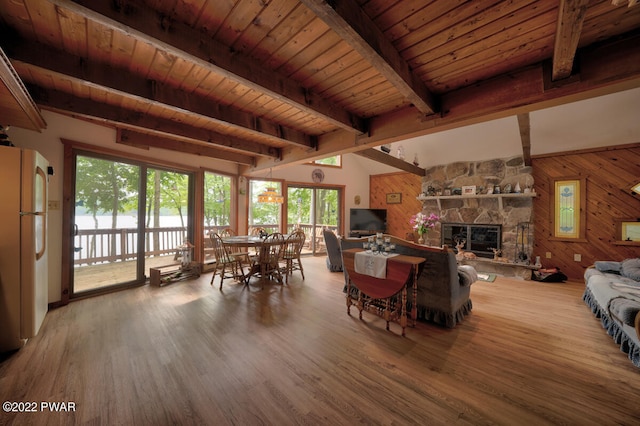 dining area featuring wood ceiling, wooden walls, hardwood / wood-style flooring, beamed ceiling, and a stone fireplace